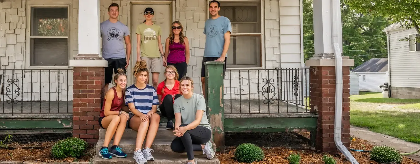 A group of people posing in front of a white campus house.